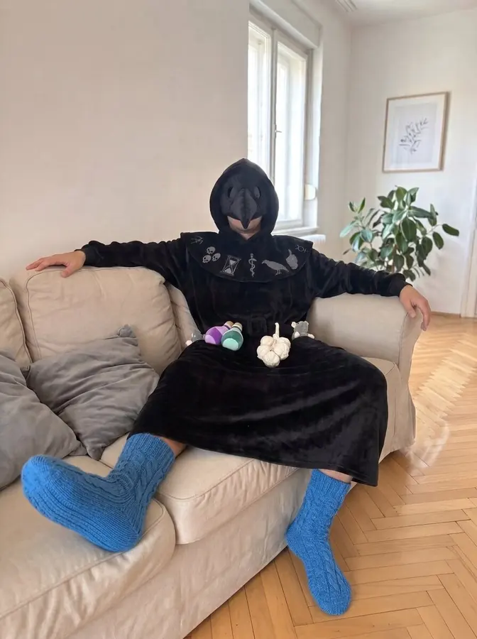 Person relaxing on a couch with tea wearing the CozyRelic Plague Doctor robe
